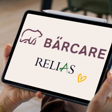 Frau hält ein Tablet in den Händen, auf dem die Logos von Bärcare und Relias mit einem gelben Herzsymbol angezeigt werden