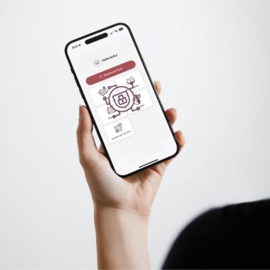 Eine Person hält ein iPhone in der Hand, auf dem eine App-Oberfläche für ambulante Pflegedienste angezeigt wird. Der Bildschirm zeigt eine Begrüßung („Hallo Sofia!“), einen großen Button „Arbeitszeit Start“ sowie mehrere Symbole mit Beschriftungen wie „Digi“, „Lernen mit RELIAS“ und „Klienten“. Im Zentrum des Displays ist ein grafisches Datenschutzsymbol mit Schloss zu sehen, das für Datensicherheit steht. Der Hintergrund ist hell und minimalistisch.